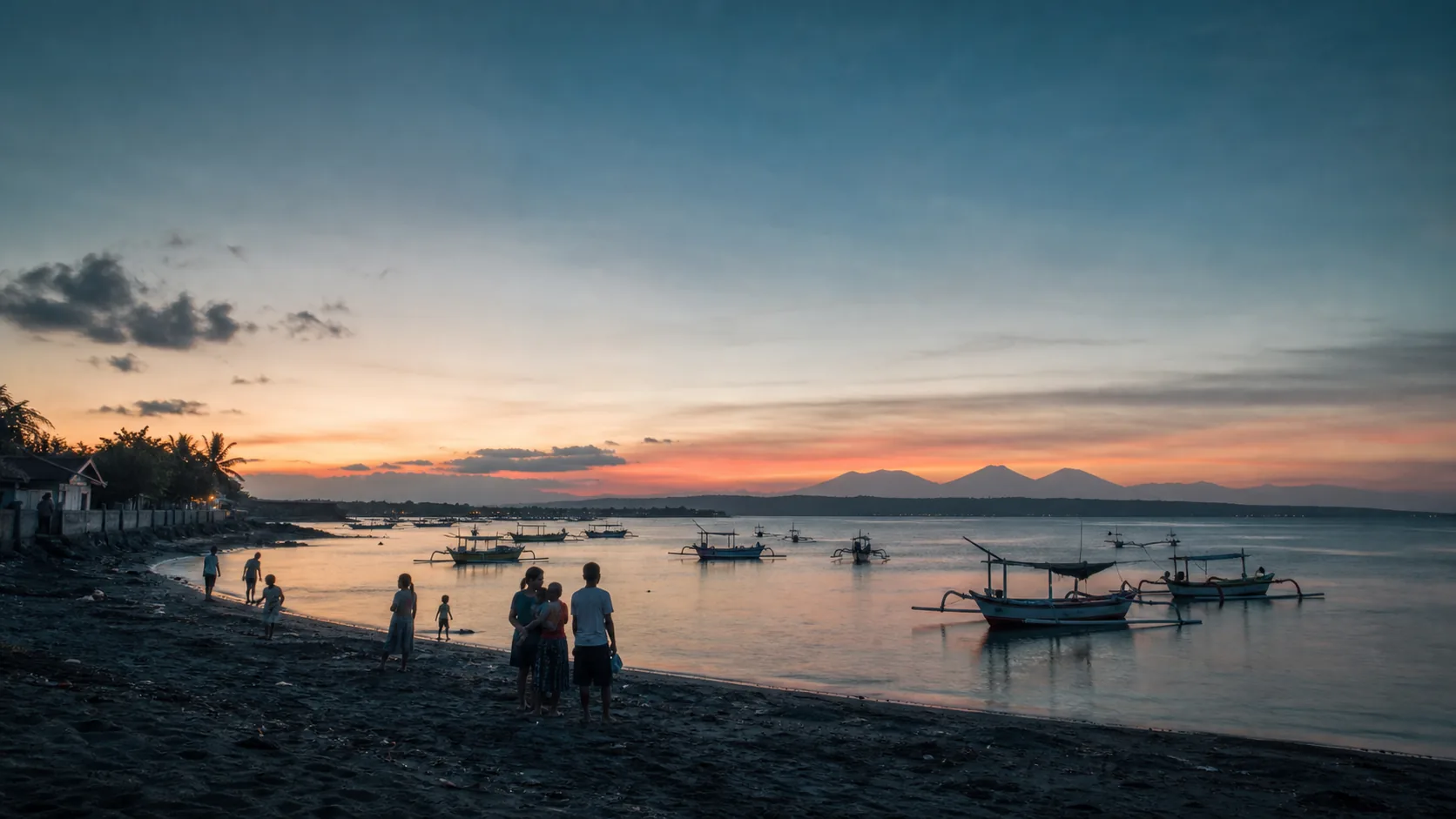Editorial evening view of local families, fishing boats and mountains along a Bali shoreline
